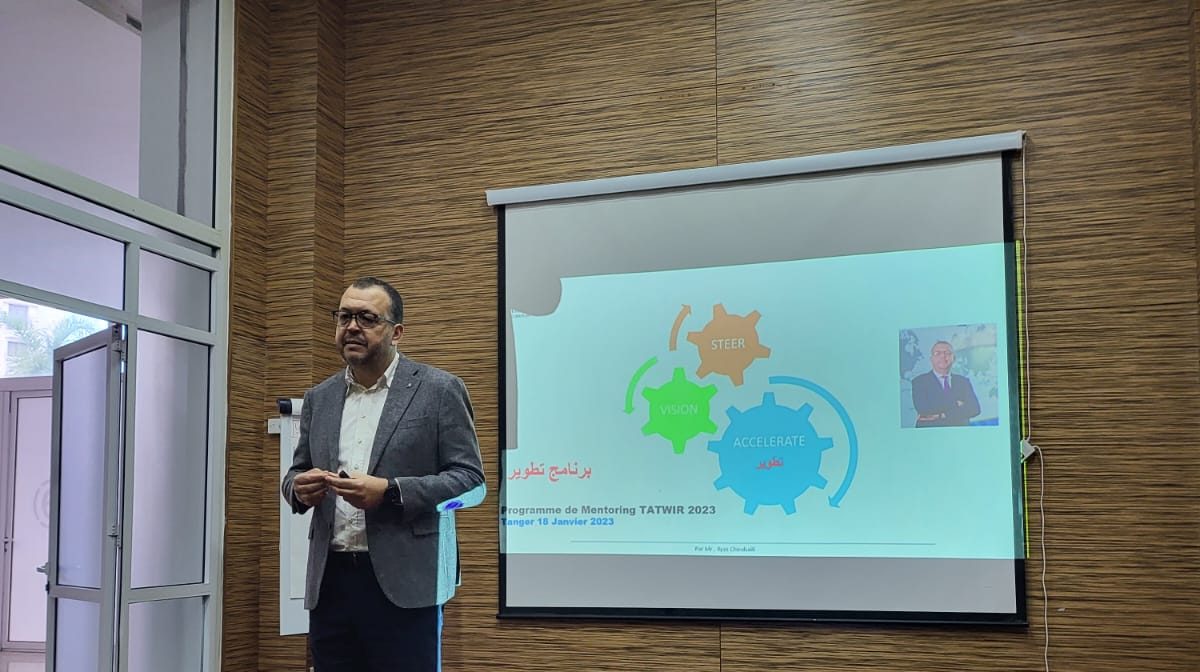 Ilyas Choubaili opening the TATWIR 2023 mentoring programme in Tangier, beside the projected programme slide.