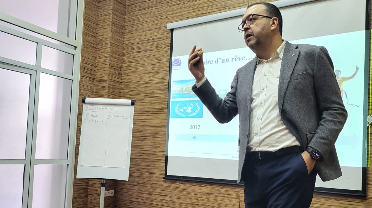 Ilyas Choubaili speaking in front of a projected slide during a workshop.